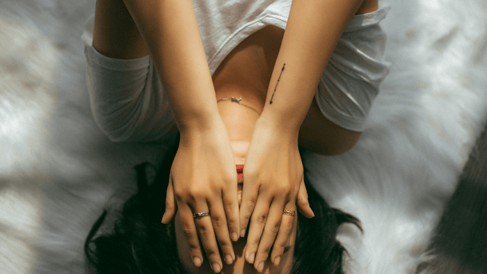 Une femme est allongée sur le lit et se couvre le visage de ses mains – expression de douleur ou d'épuisement
